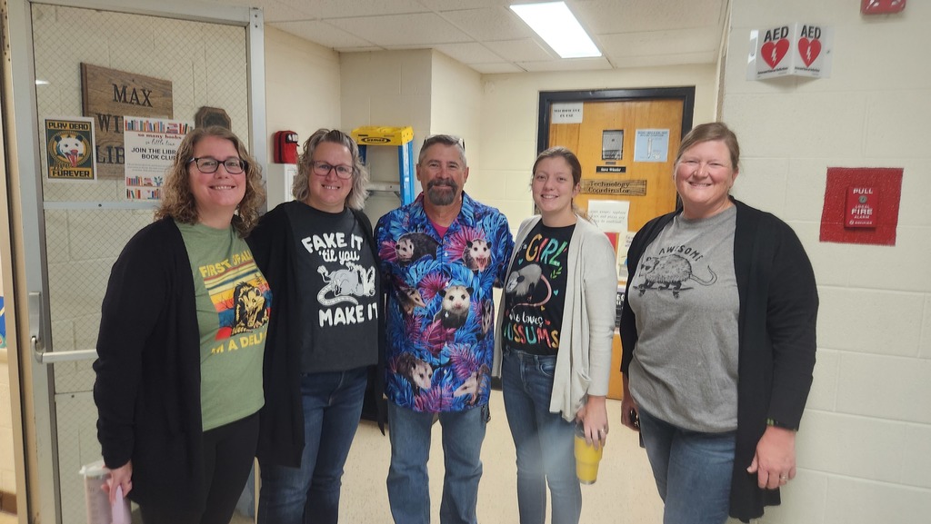 Five teachers are standing side by side. Each is wearing an opossom shirt for National Opossom Day.