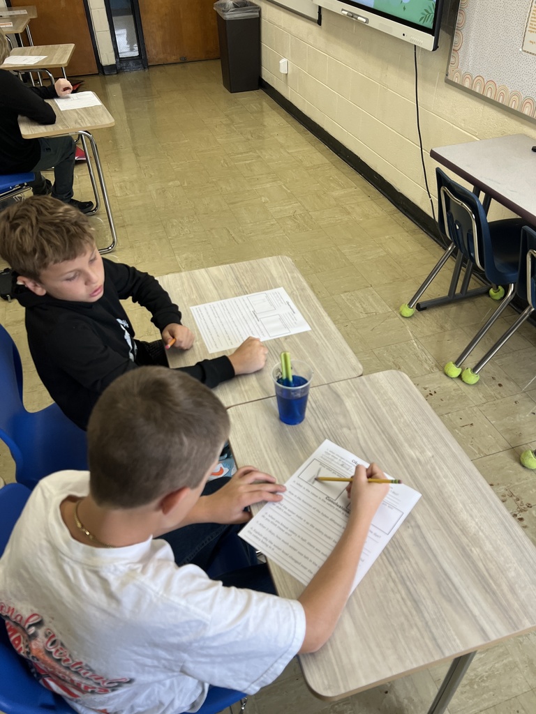 Two students are filling out their worksheet. They are observing a celery stalk in a cup of blue dyed water. 