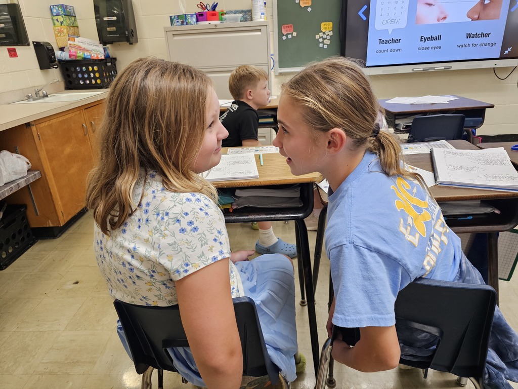 Two students are sitting a foot apart. One is staring at the other. The second has just opened her eyes.