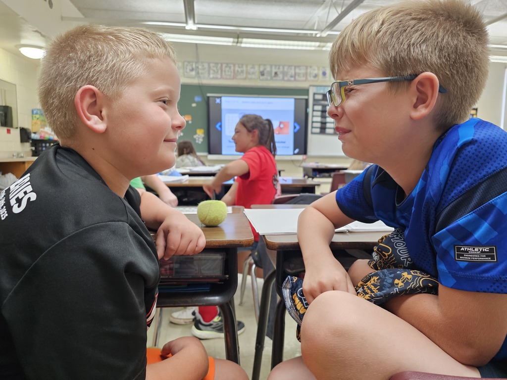 Two students are sitting a foot apart. One is staring at the other. The second has his eyes closed.
