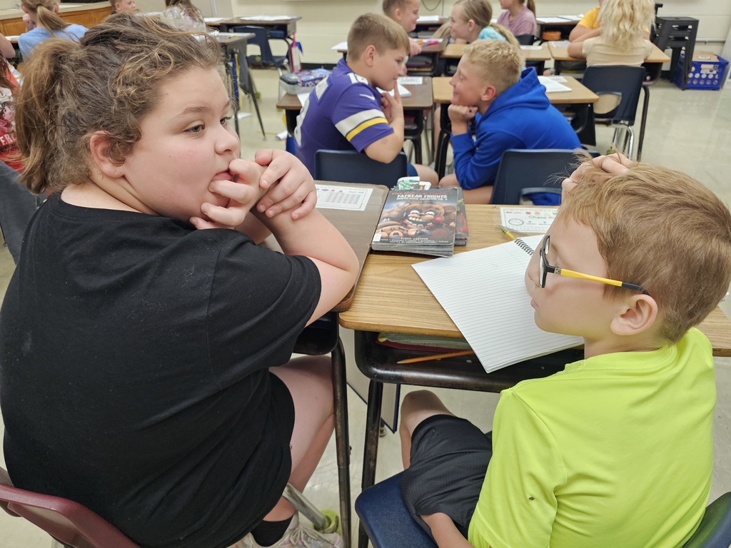 Two students are sitting a foot apart. One is staring at the other. The second has his eyes closed.