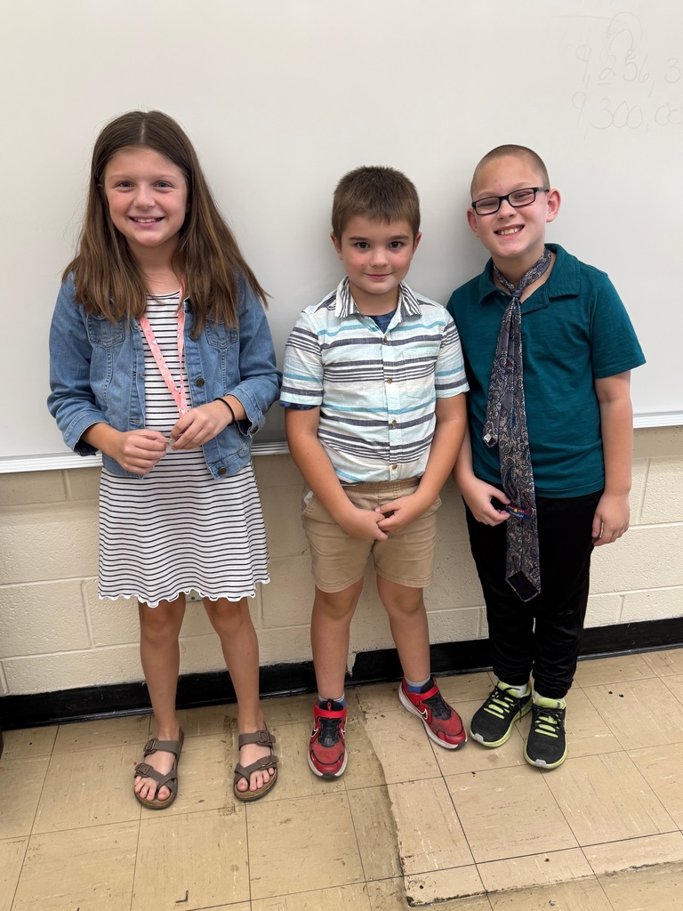 The three students are dressed as teachers. The girl has a dress and lanyard. The boys have nice shirts and shorts on. The one boy is wearing a tie.