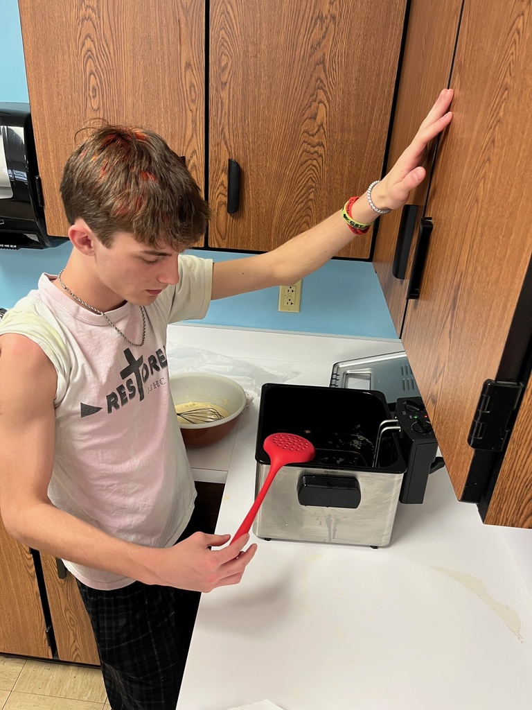 A student is standing at the counter. He has a spatula in his hand over the fryer.