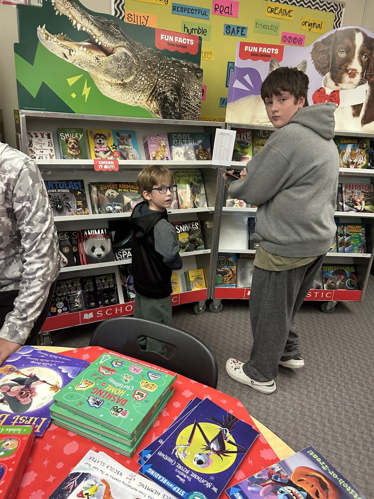 An older student is writing down  a list on the clipboard. A younger student is making a choice.