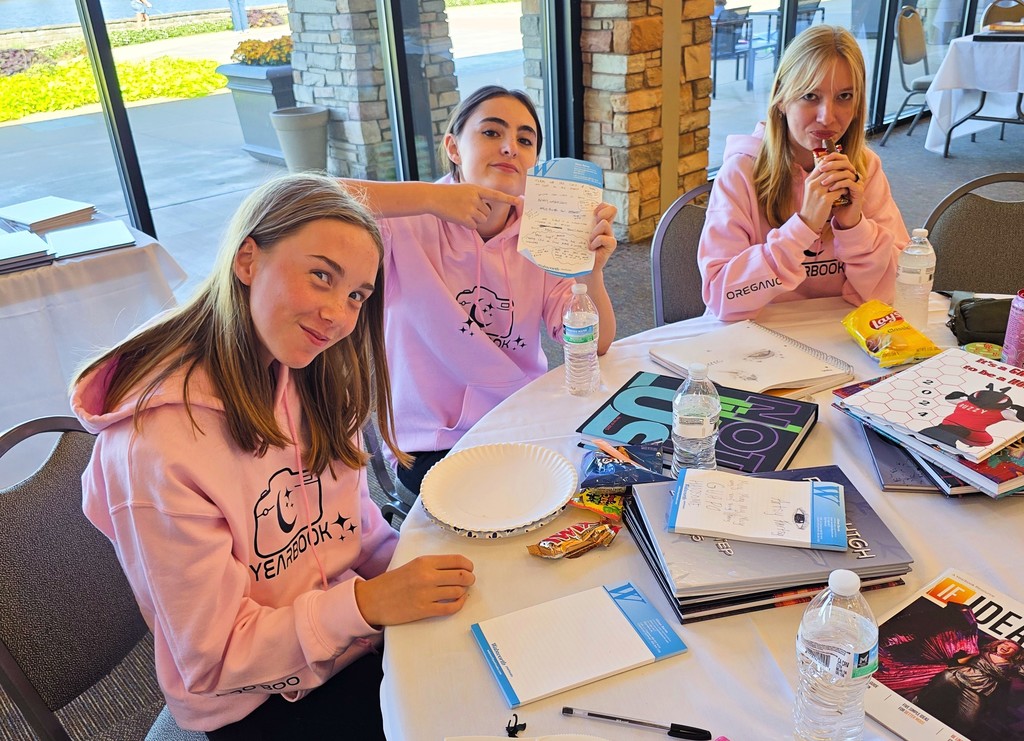 Three students are sitting at a table where they working. One student is holding up a list.