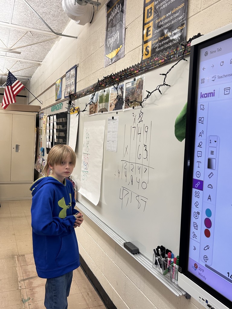 A student is standing the board. The student is working a math problem.