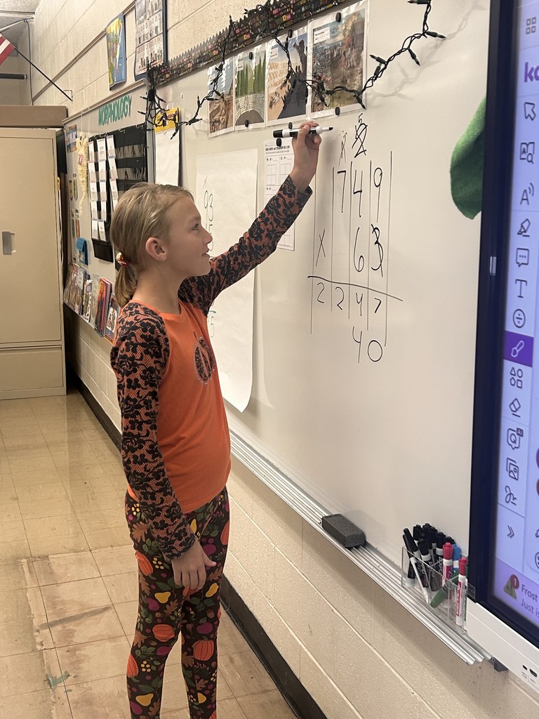 A student is standing the board. The student is working a math problem.
