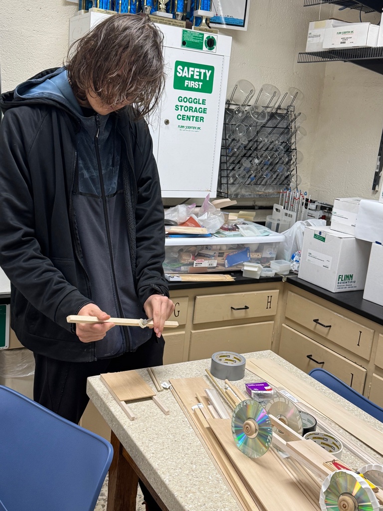A student is standing at a table. He has wood in front of him.