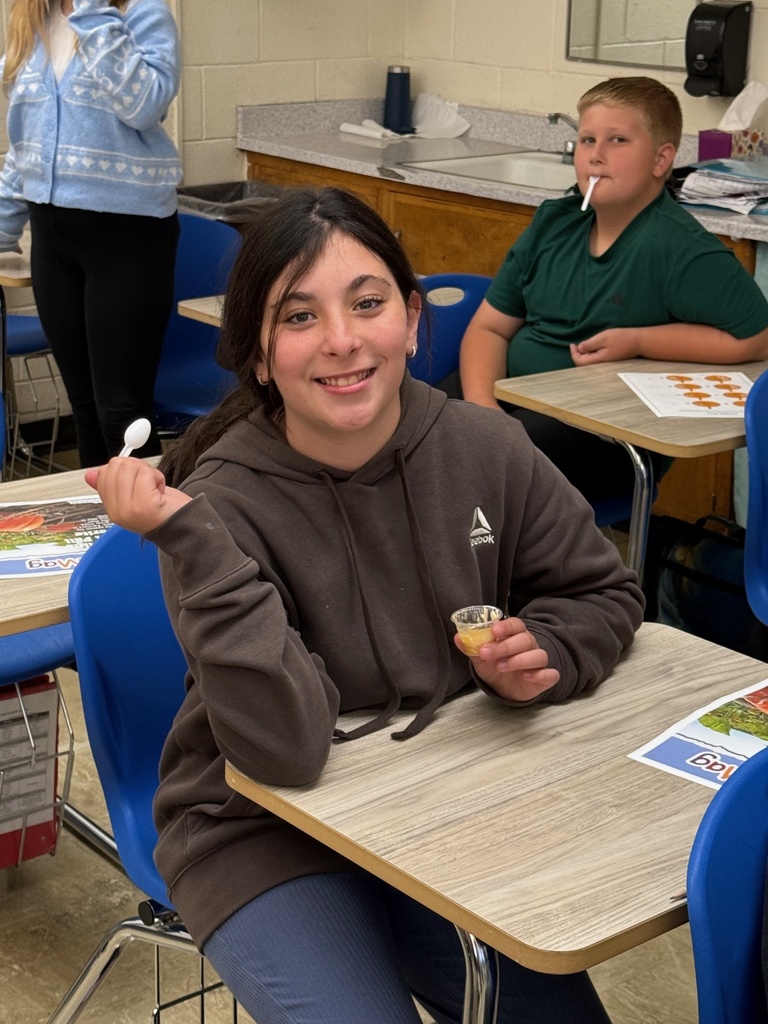 A student is sitting at a desk holding a mini cup of pumpkin pie and a mini spoon..