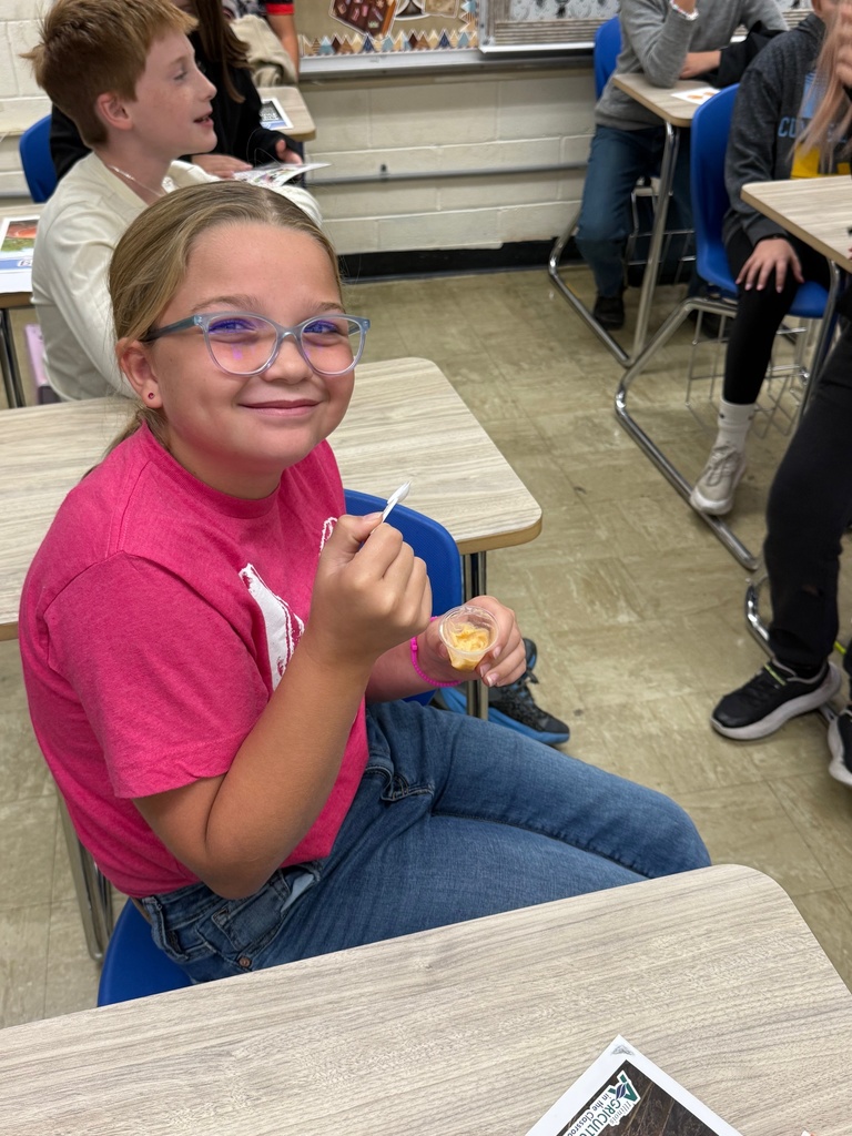 A student is sitting at a desk holding a mini cup of pumpkin pie and a mini spoon..