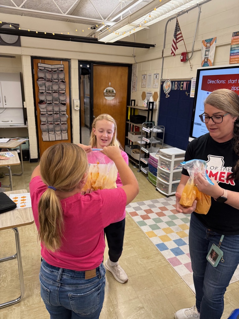 The teacher is holding an baggie full of pumpkin filling. Two girls are holding another bag.