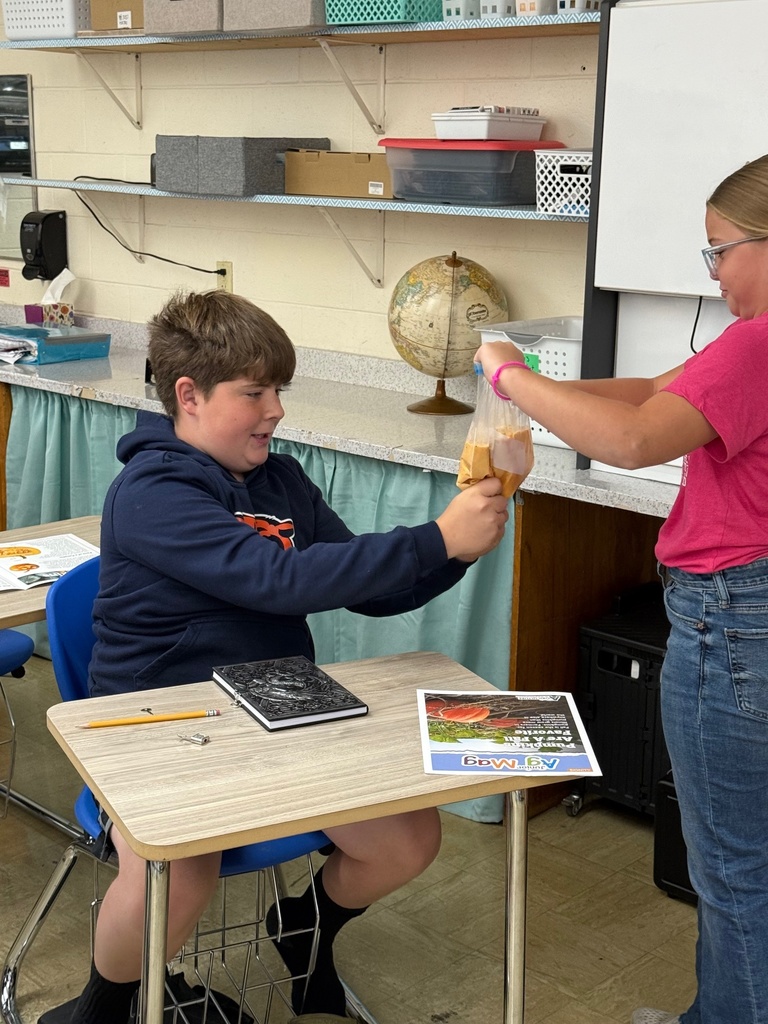 A girl is standing holding a bag of pumpkin filling. Another student is squeezing the bag.