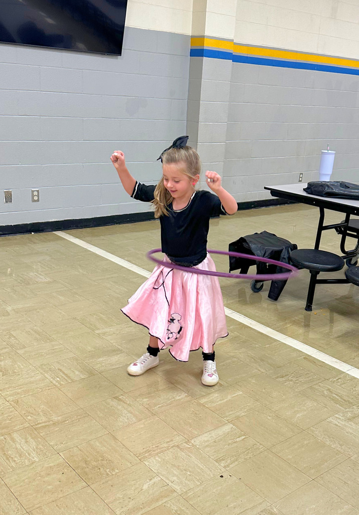A student is dressed in 50s attire. She is hula hooping.