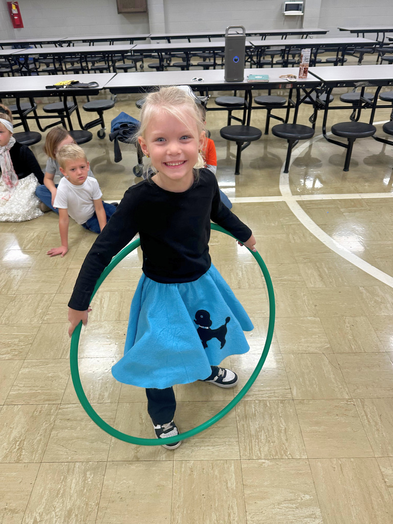 A student is dressed in 50s attire. She is hula hooping.