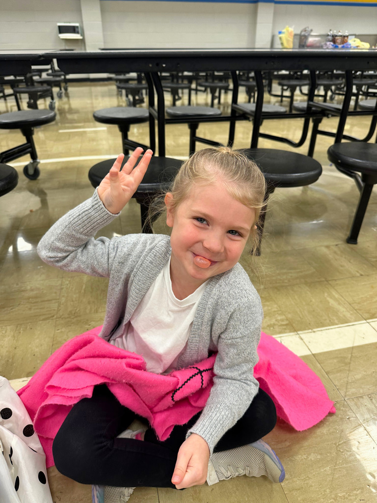 A student is dressed in 50s attire. She is blowing bubble.