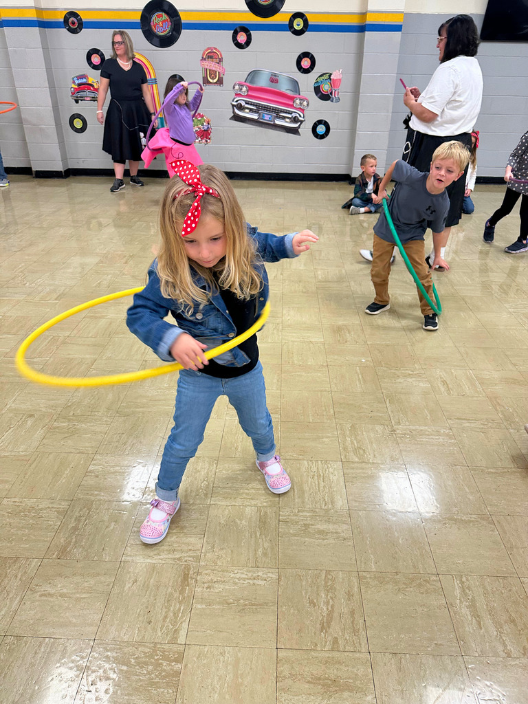 A student is dressed in 50s attire. She is hula hooping.