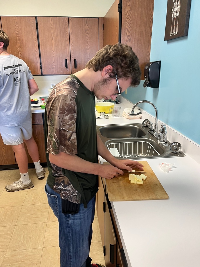A student is standing at the counter dicing apples on a cutting board.