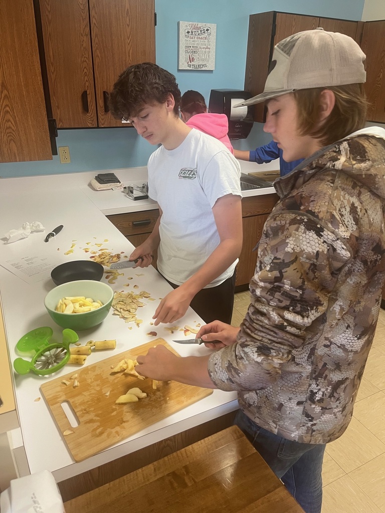 Two students are standing at a counter. One is pealing apples and the other is dicing them.