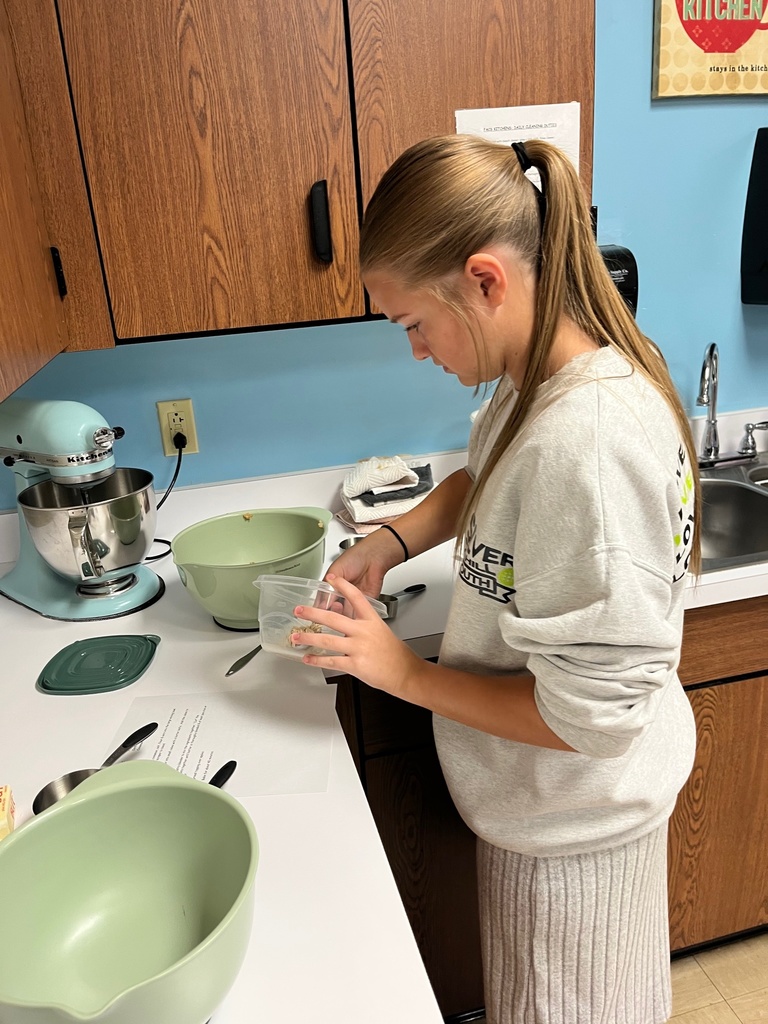 A student is standing at the counter. She is holding a bowl and is mixing something in it.