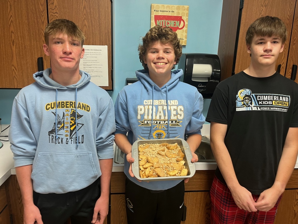 Students are standing side by side. The middle student is holding the pan of apple crisp.