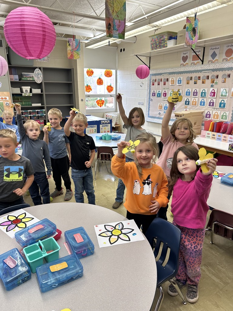 A group of nine students are holding up their pollenation puppet. These are paper bees glued on the end. to a clothes pin with a cotten ball on the end.