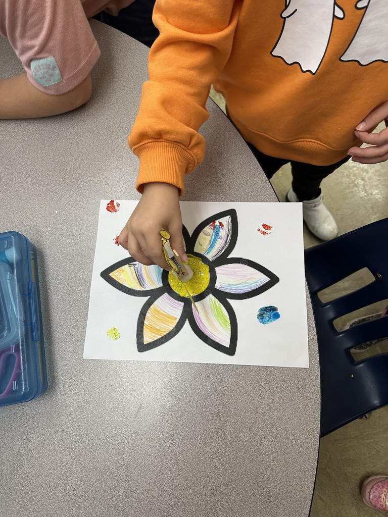 A student is dipping the pollenation puppet into "pollen" on a flower. Then, the student touches it on the paper to show the transfer.