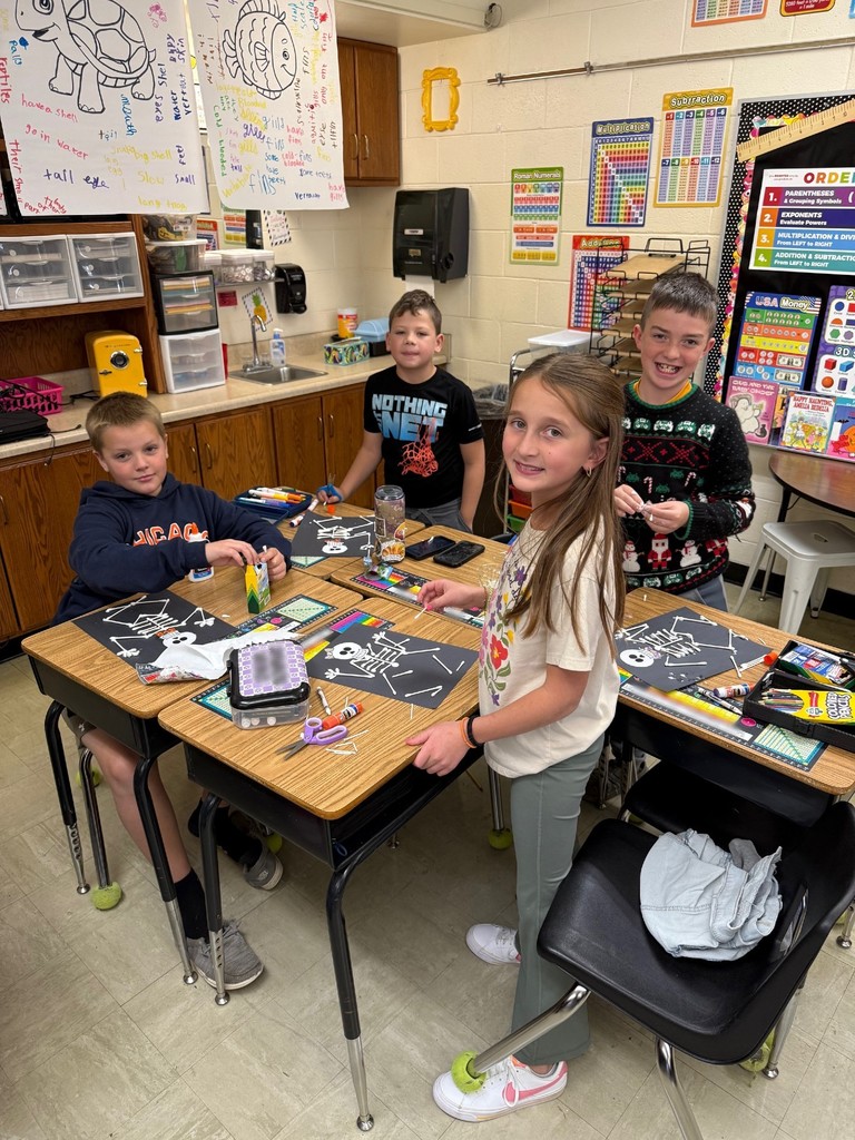 Students are standing at their desks. On the desk are the skeletons they are making.