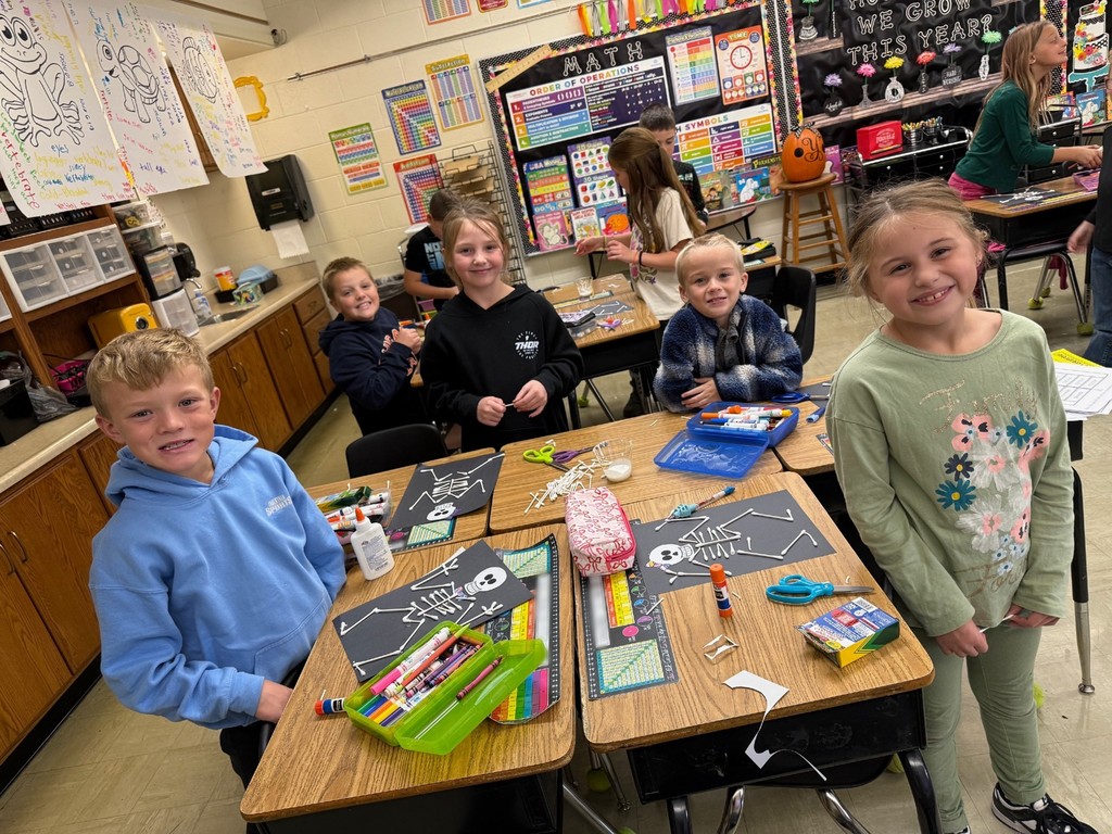Students are standing at their desks. On the desk are the skeletons they are making.