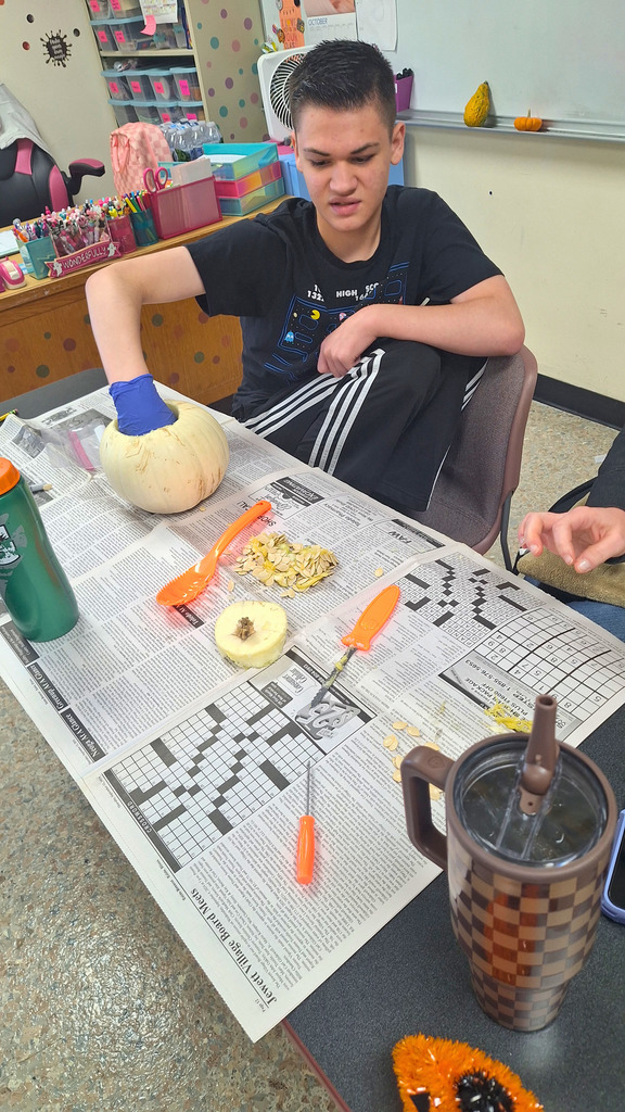 The student is sitting at a table covered in newspaper. He is digging out th e seeds.