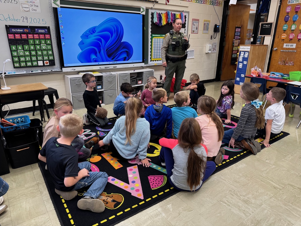 Students are sitting on the class carpet. . SRO Elizabeth is listening to a student.