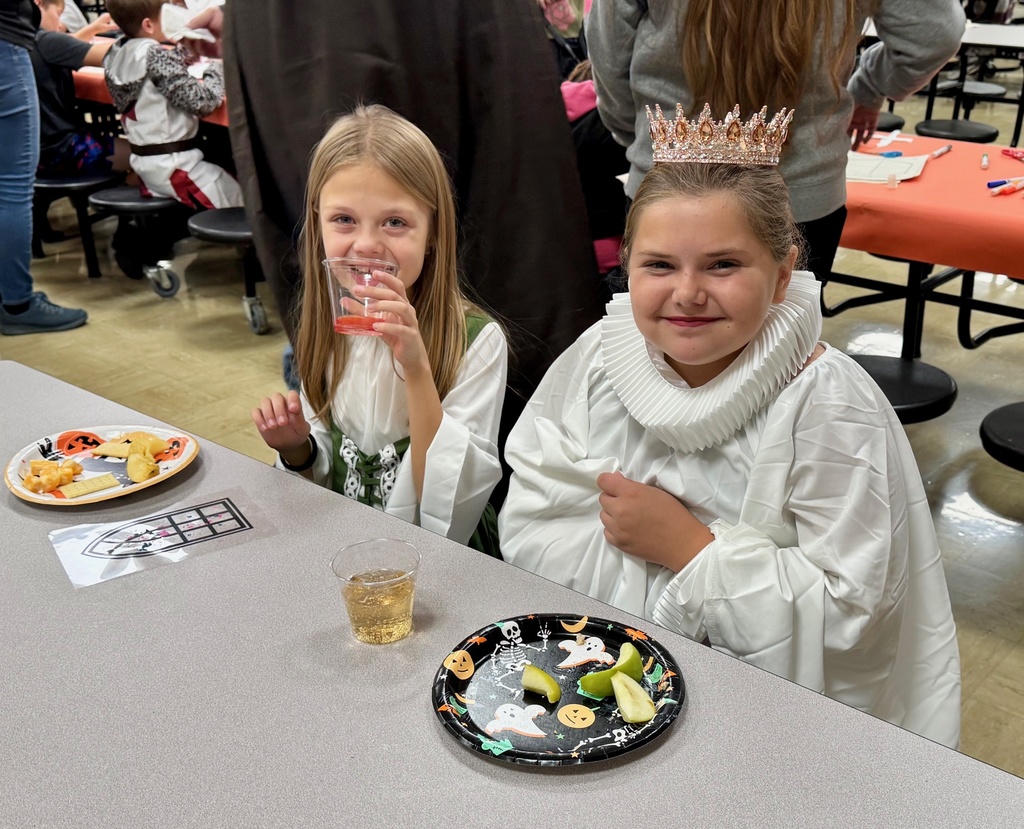 Two students are sitting at the table having a snack. They are dressed as medieval people.