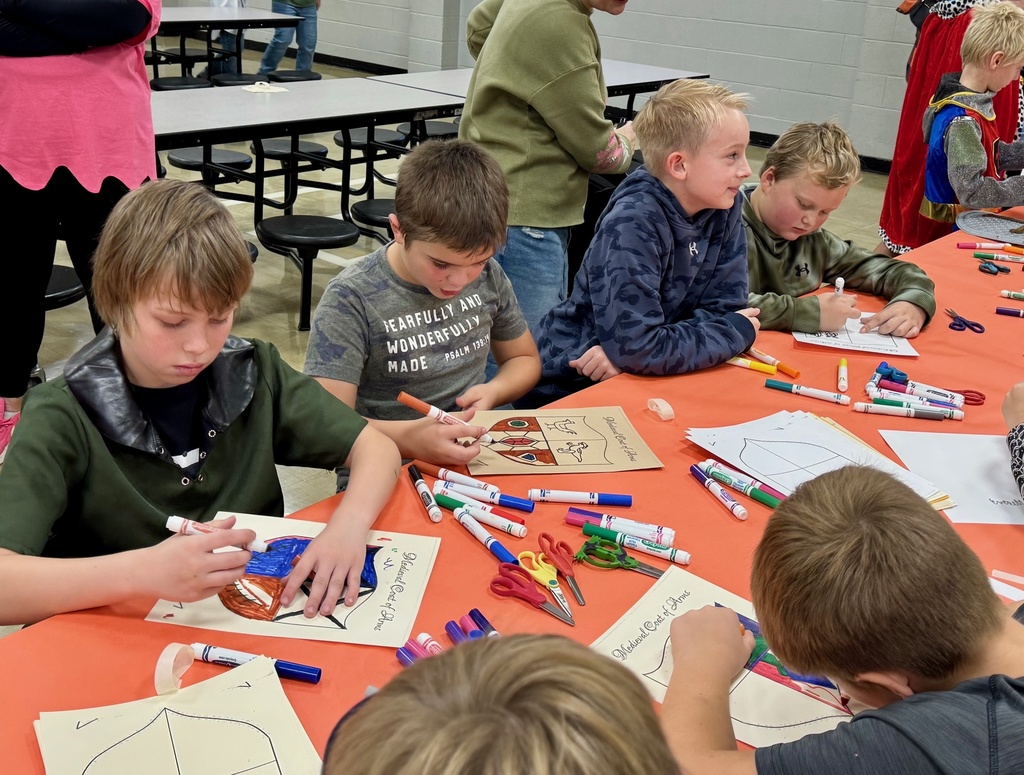 Several boys are sitting at a table. They are decorating their crests.