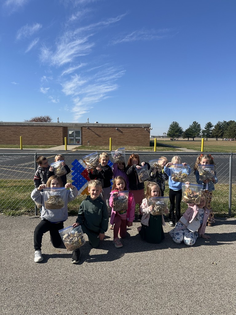 The class is standing by the fence. They are each holding a baggie of their leaf collection.