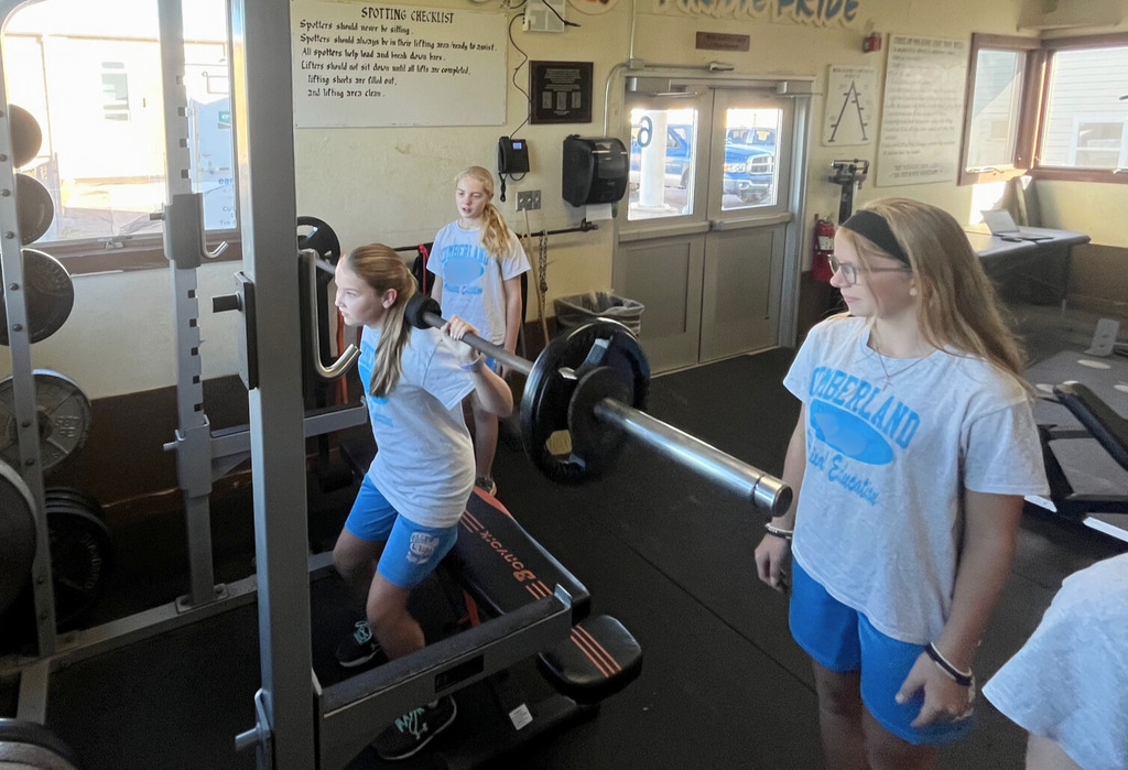 A student is doing a dead lift. Two other students are spotting that student.