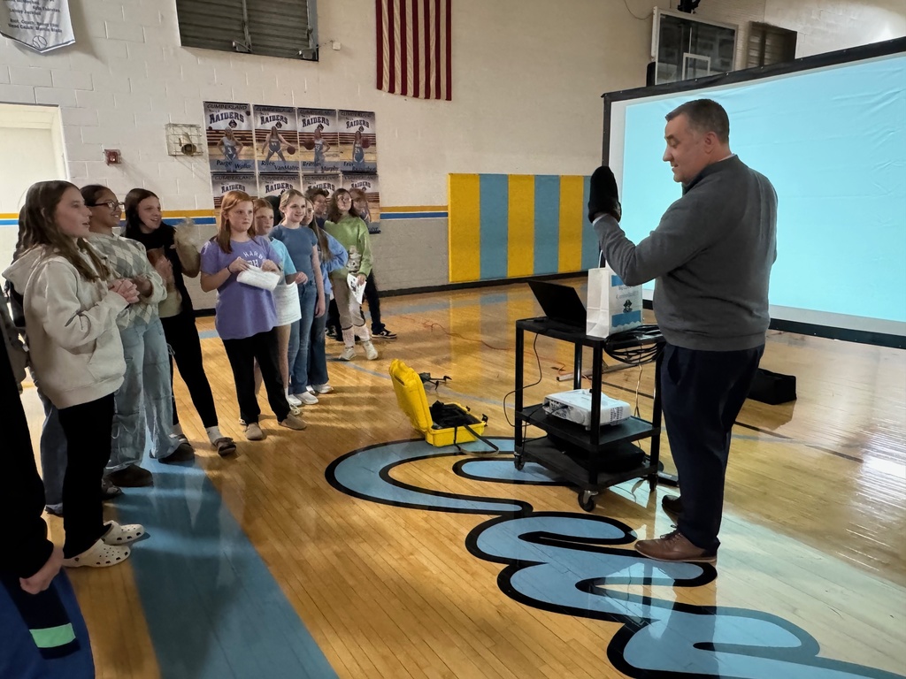 The students are watching as Kevin checks out the Cumberland beanie that they got him. 