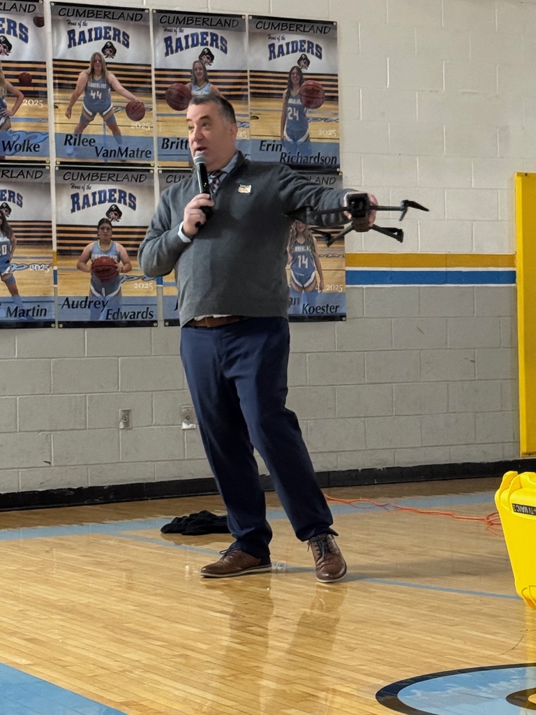 Mr. Lighty is speaking to the group in the gym. He is showing them the drone.