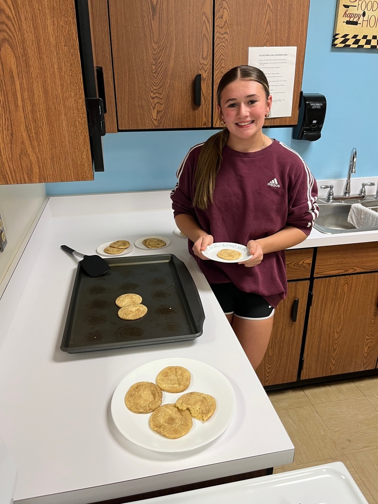 A student is standing at the counter. She has a plate with a snickerdoodle on it. She is dishing some cookies on to her plate. 