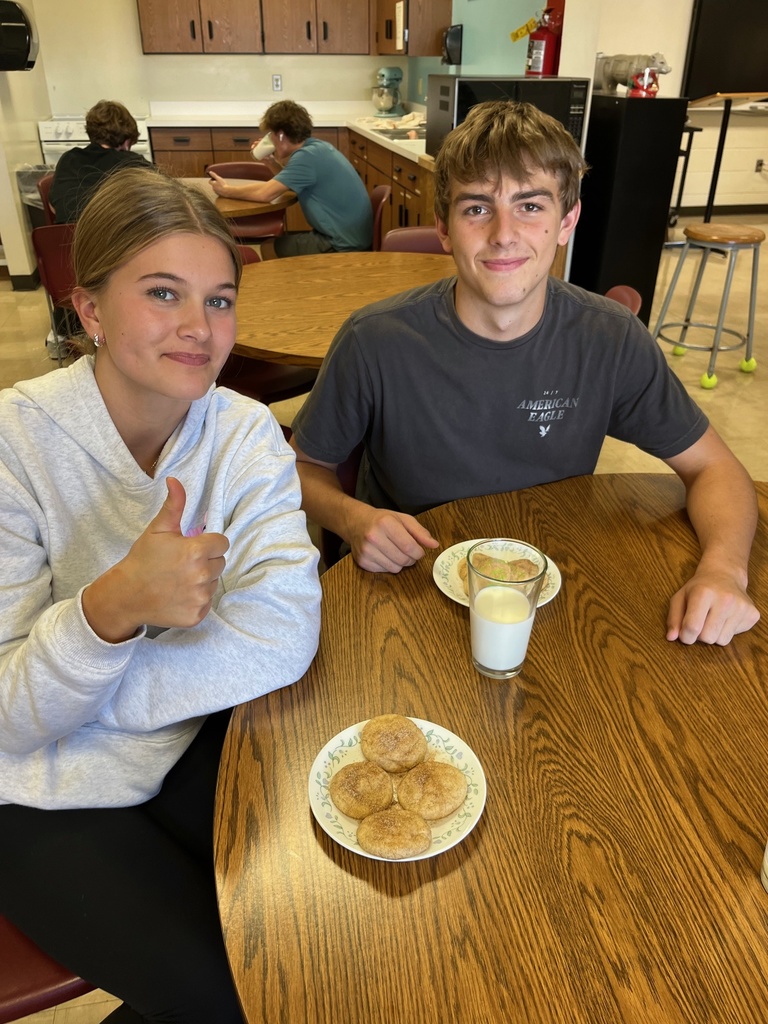 Two students are sitting at a table They each have snickerdoodles on their plates. One has a glass of milk, too. 