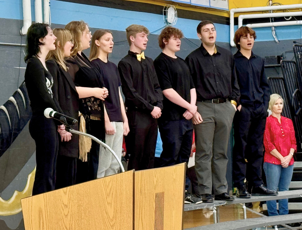 The high school vocal group is singing the Star Spangled Banner. They are standing on risers.