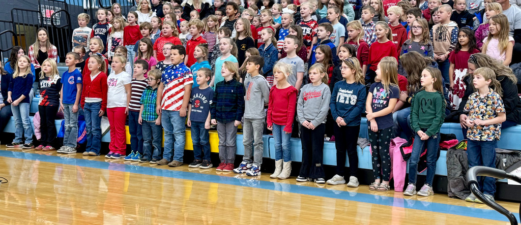The elementary students are standing in the bleachers. They are singing a song.