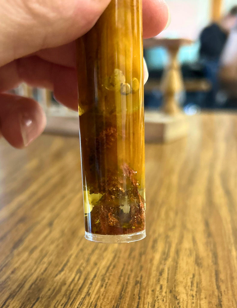 Shown is a test tube. The contents are brown in color. There are crystals growing. 