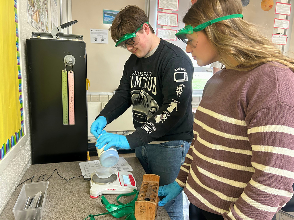 Student are wearing safety goggles and gloves. They are scooping something out of a container.