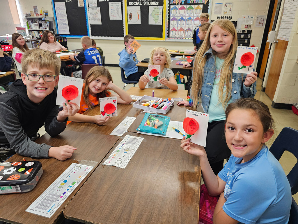 Students pictured are showing their cards to veterans. They have a poppy on the front. They say thank you for your service.