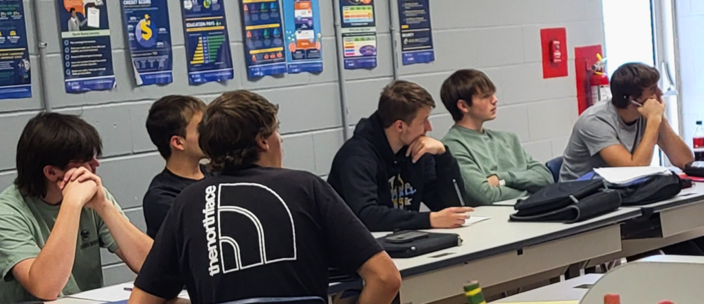 The students are sitting at their tables facing the screen. They are watching the documentary. 