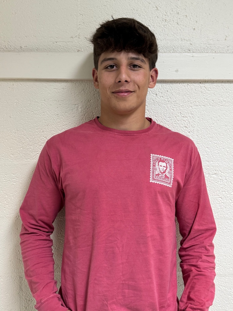 Pictured is Owen. He is wearing a pink shirt and is standing in front of a white wall.