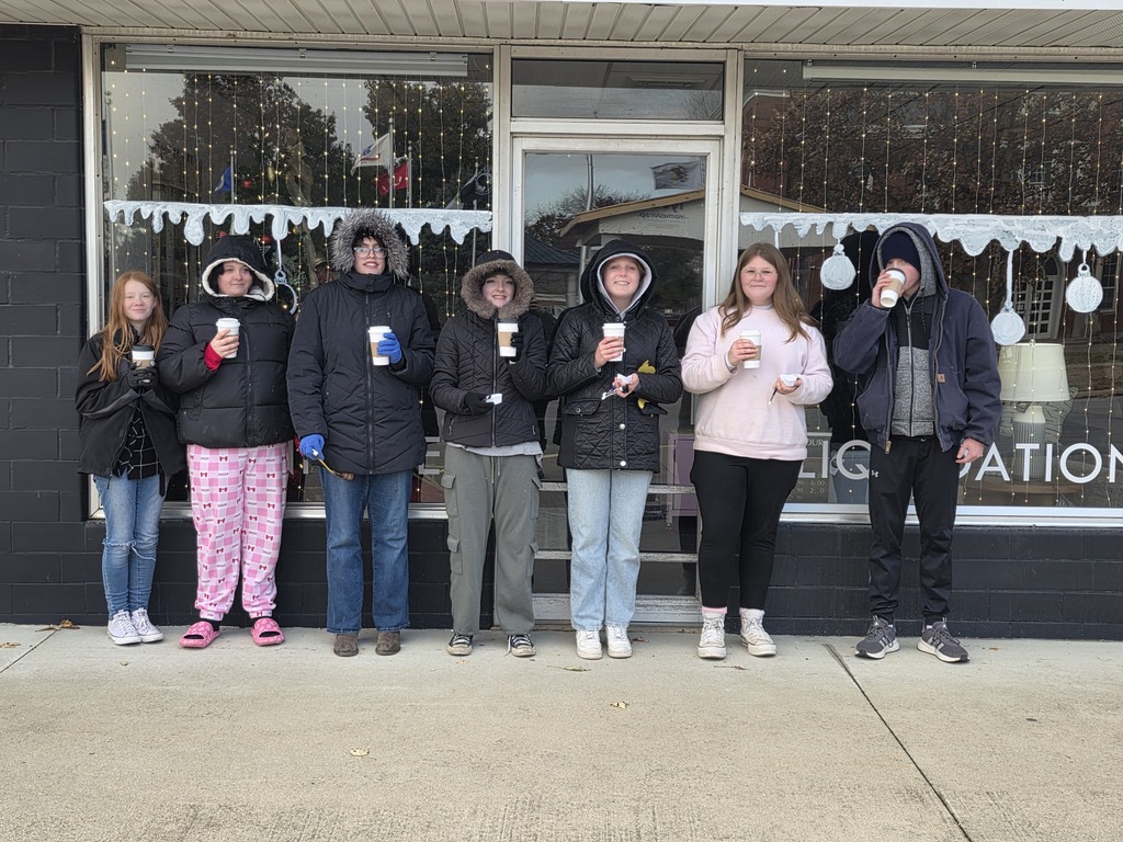 Five students are standing in front of a window that they just painted in a Christmas theme.