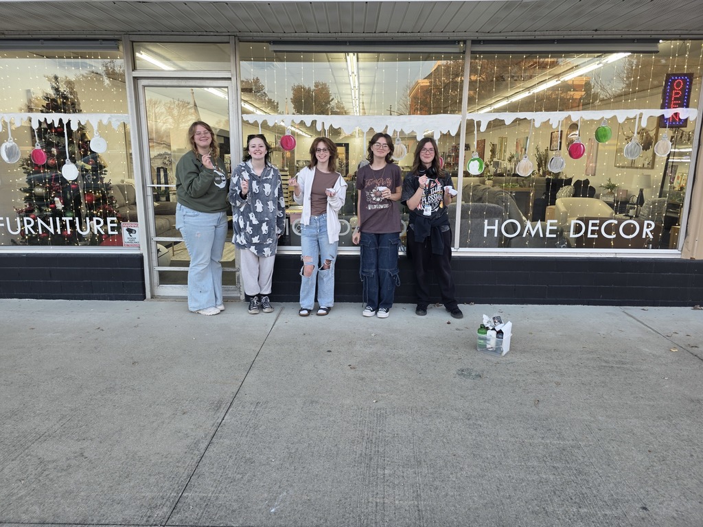 Five students are standing in front of a window that they just painted in a Christmas theme.