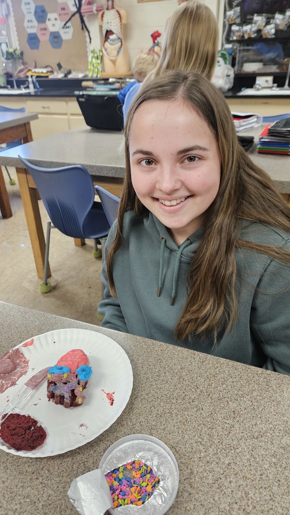 A student is displaying their model of the heart. It has red and blue icing to show the chambers.