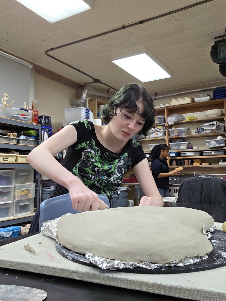 A student is molding clay in to a larg heart shape.