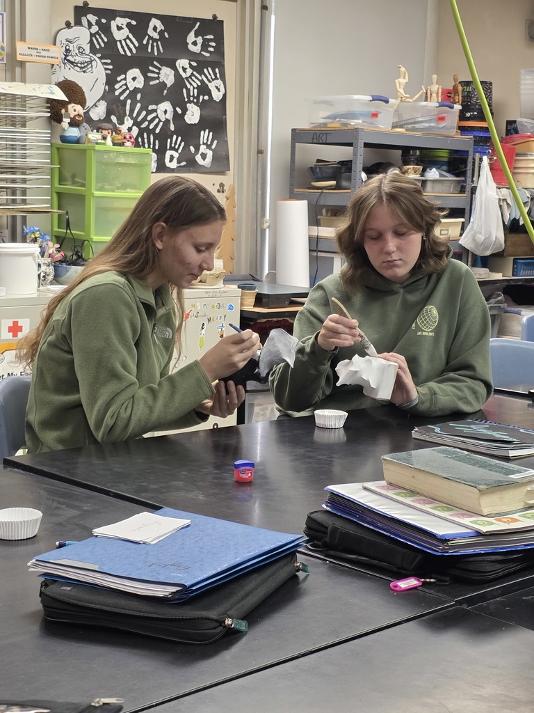 Two students are painting their sculptures. They are both white.